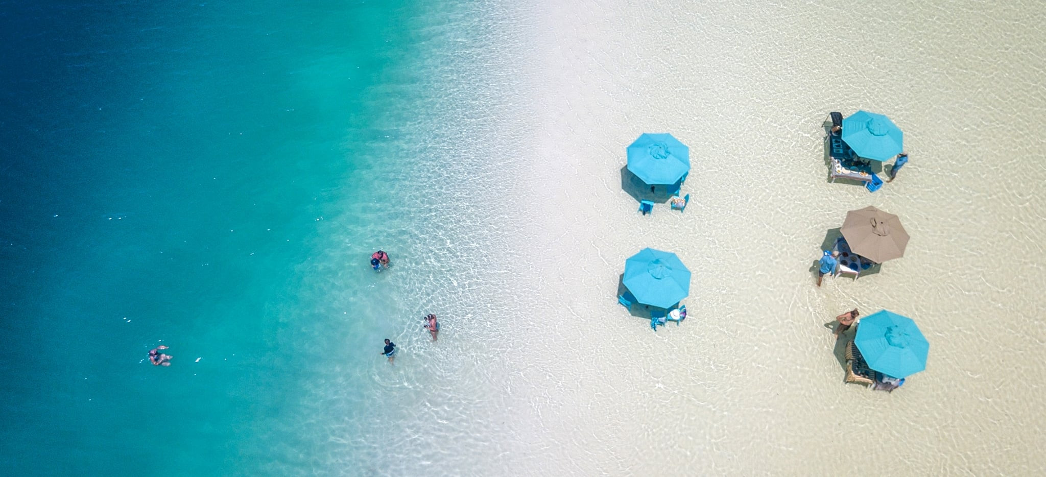 Ein weißer Sandstrand auf einer Snadbank Nahe Alphonse, Sonnenschirme und Menschen baden im türkisen Meer